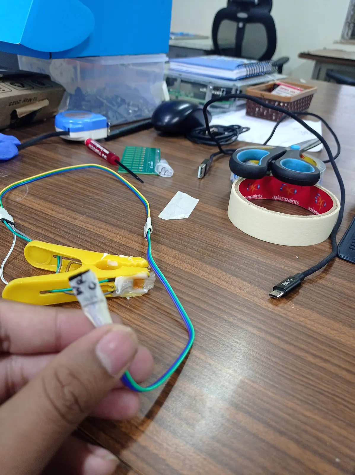 No FPC adapter anywhere in the building, so a clothes peg became the connector — jaws clamp the flex cable, wires soldered onto the contacts.
